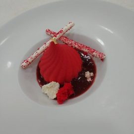 Μους φράουλας ψεκαστό πάνω σε Ντακουάζ φιστικιού με κουλί λευκής σοκολάτας, κονφί φράουλας και γαλλική μαρέγκα.