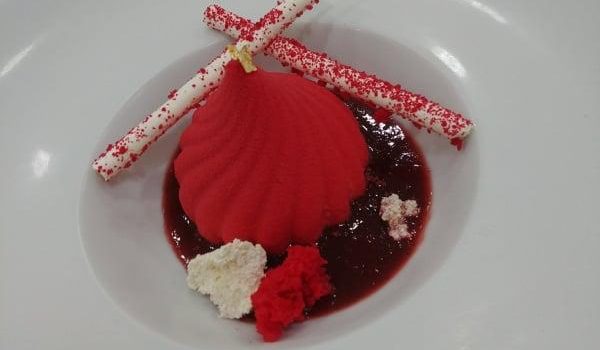 Μους φράουλας ψεκαστό πάνω σε Ντακουάζ φιστικιού με κουλί λευκής σοκολάτας, κονφί φράουλας και γαλλική μαρέγκα.